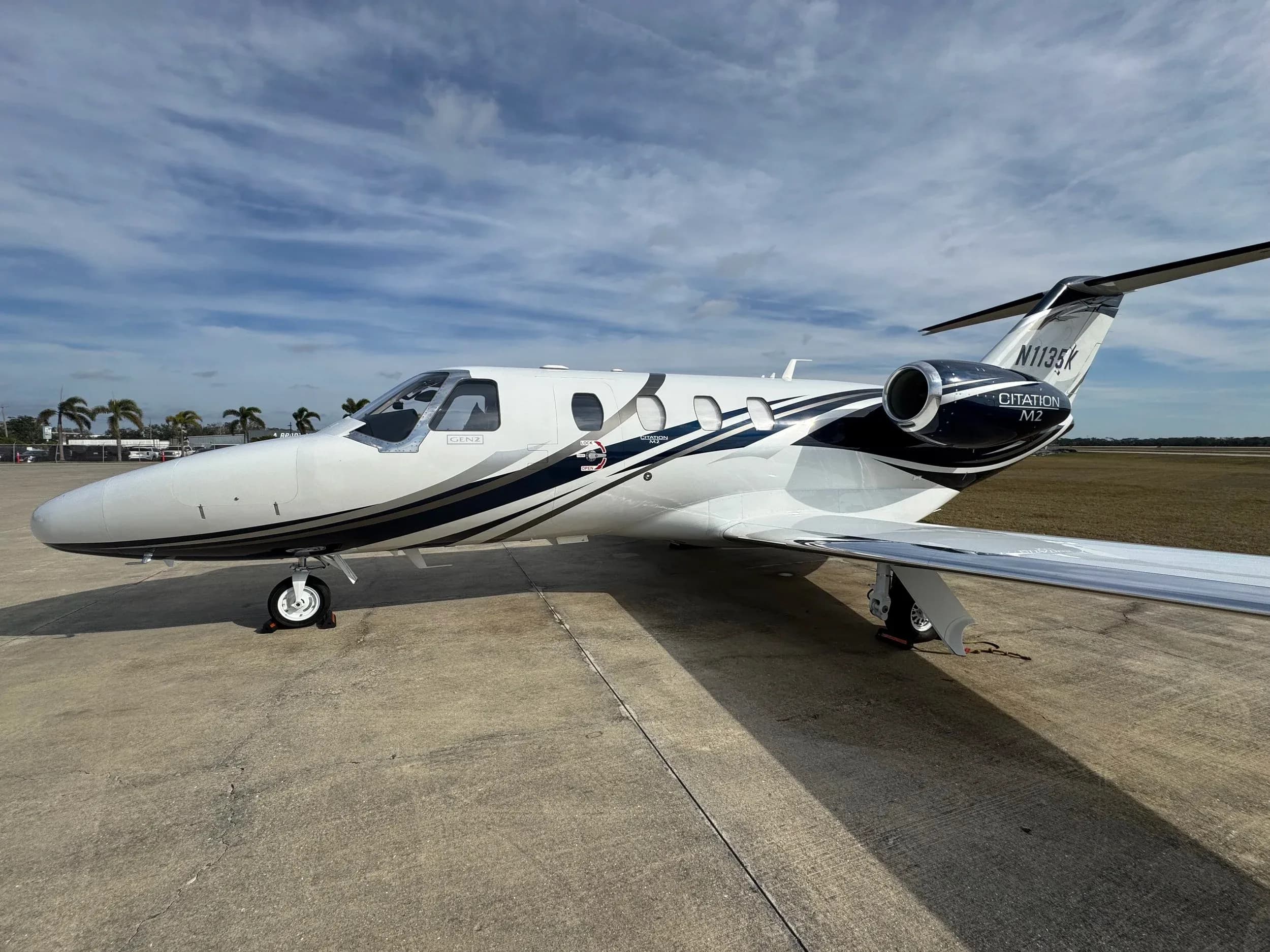 A Citation M2 jet with a white and black paint scheme is parked on the tarmac.