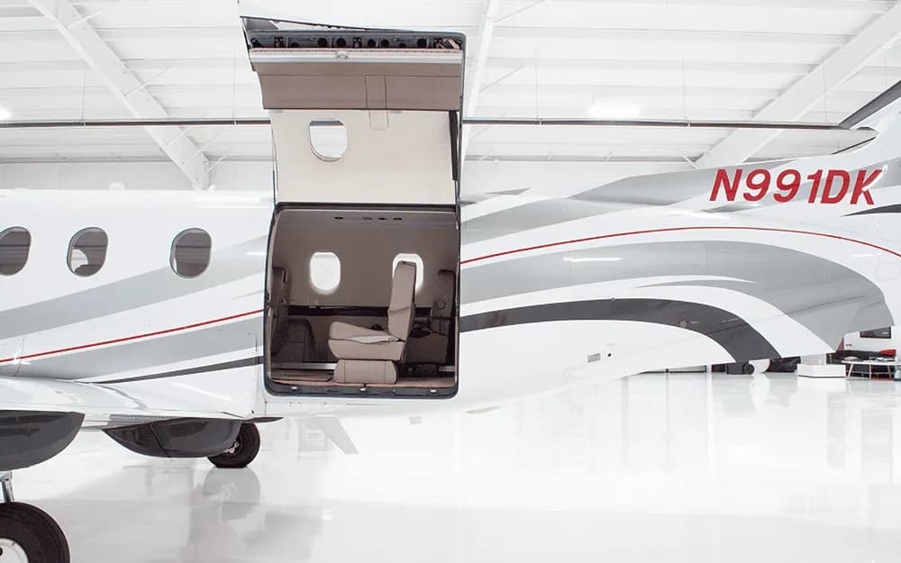 The rear fuselage of a white Pilatus PC-12 aircraft with its large cargo door open, showing a glimpse of the cabin.