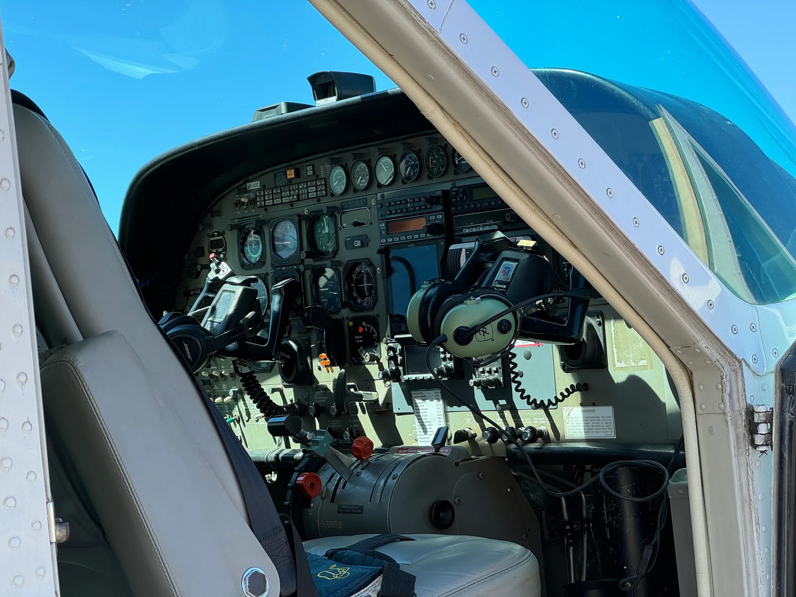 The cockpit of a small aircraft, showing the instrument panel, yokes, and throttle quadrant, viewed through an open door.