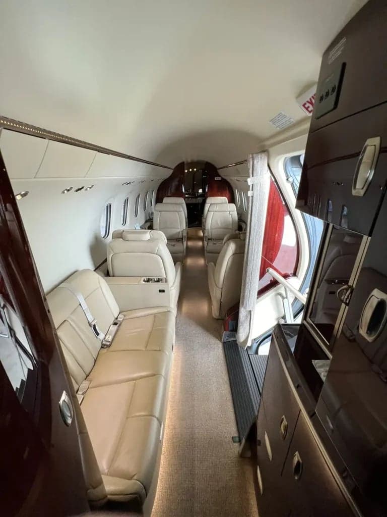 A view down the aisle of the aircraft cabin, showing the seating arrangement and wood trim.