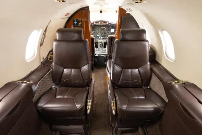 Interior view of the Learjet 45XR cabin with leather seats and tables facing the cockpit.