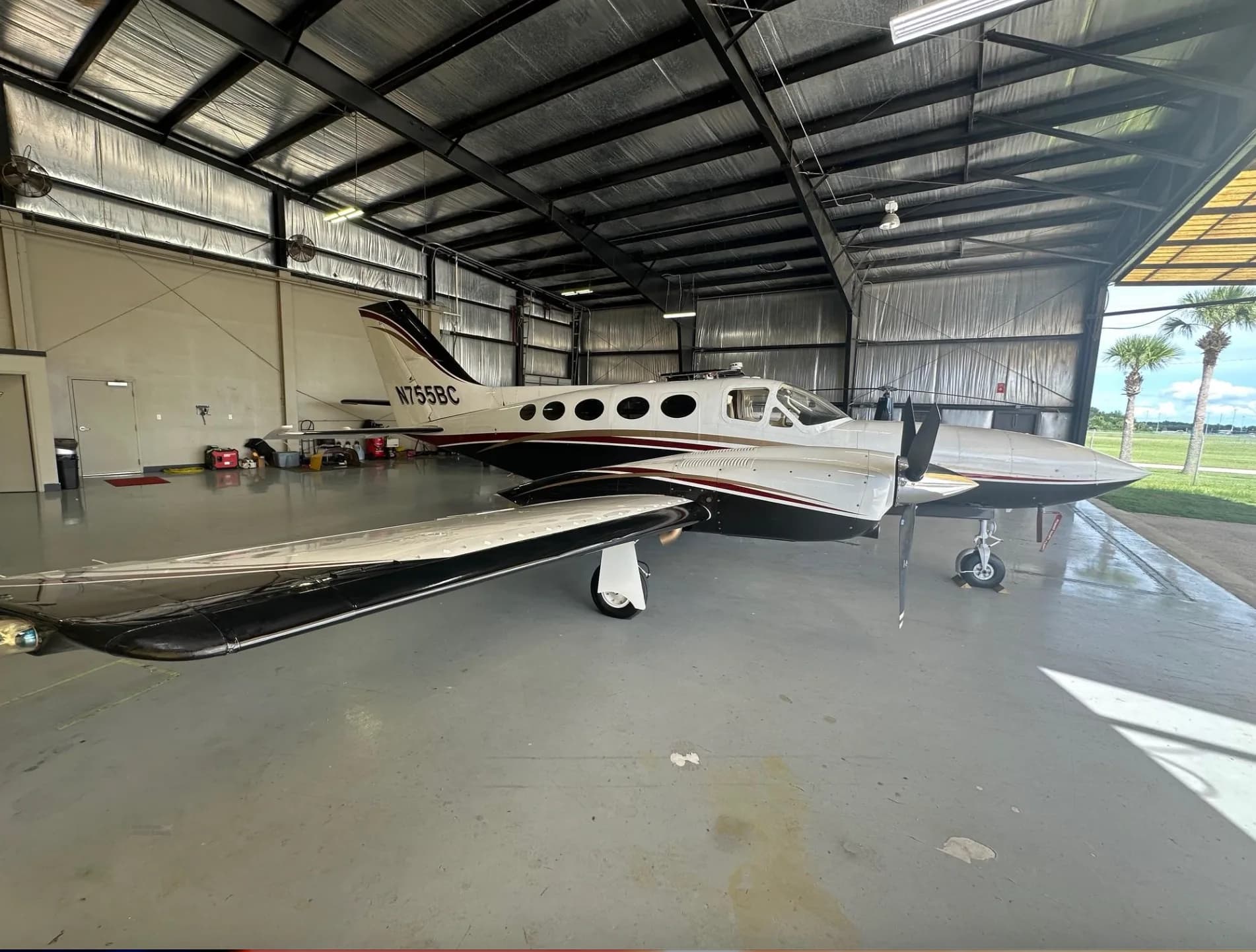 A white, black, and red twin-engine turboprop aircraft, N755BC, parked inside a hangar, viewed from the side.