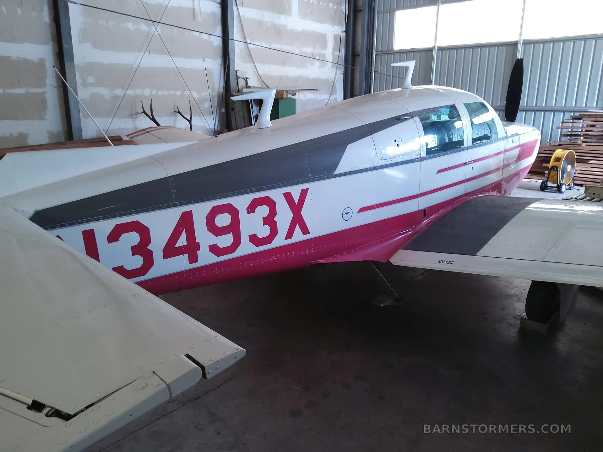 Rear-side view of a white and red single-engine aircraft with registration N3493X, parked in a hangar.