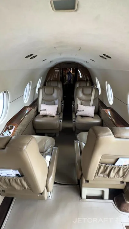 The interior cabin of a business jet, featuring tan leather seats arranged in a club configuration.