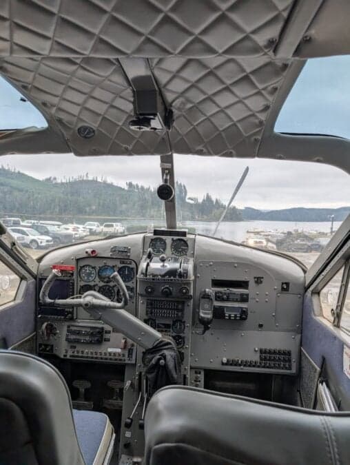 The cockpit of a de Havilland Beaver floatplane with a view of the lake.