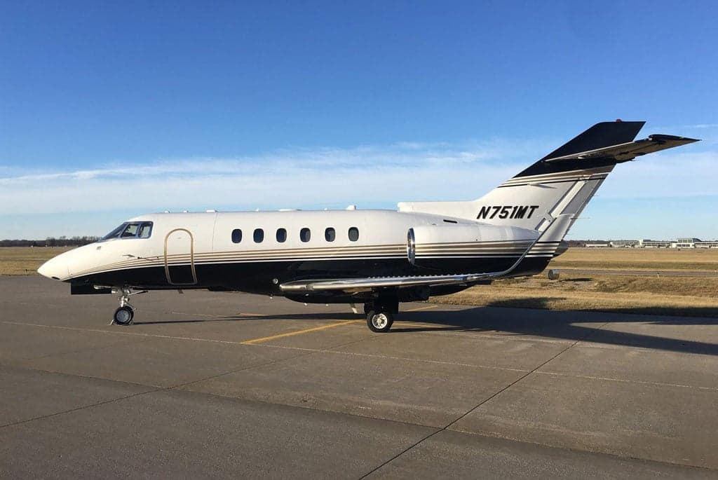 A full side view of the N751MT business jet, featuring its white, black, and gold striped livery, parked on a concrete tarmac.