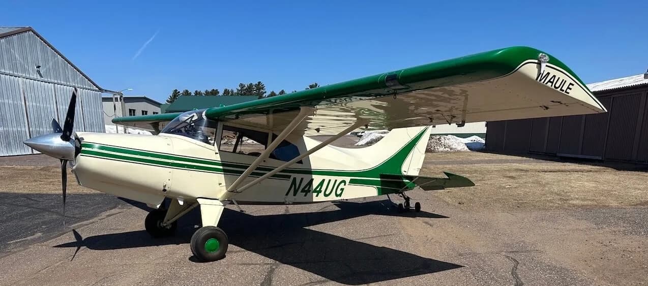 A Maule aircraft with a green and white paint scheme is parked on an asphalt airfield.
