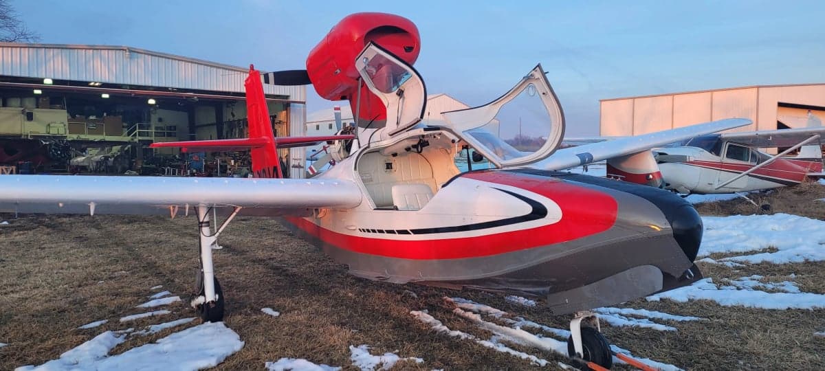 A Republic RC-3 Seabee aircraft with an open door is parked on the grass with snow.