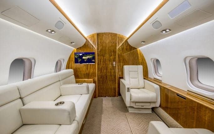Interior view of the aircraft cabin with white leather seating and wood trim.