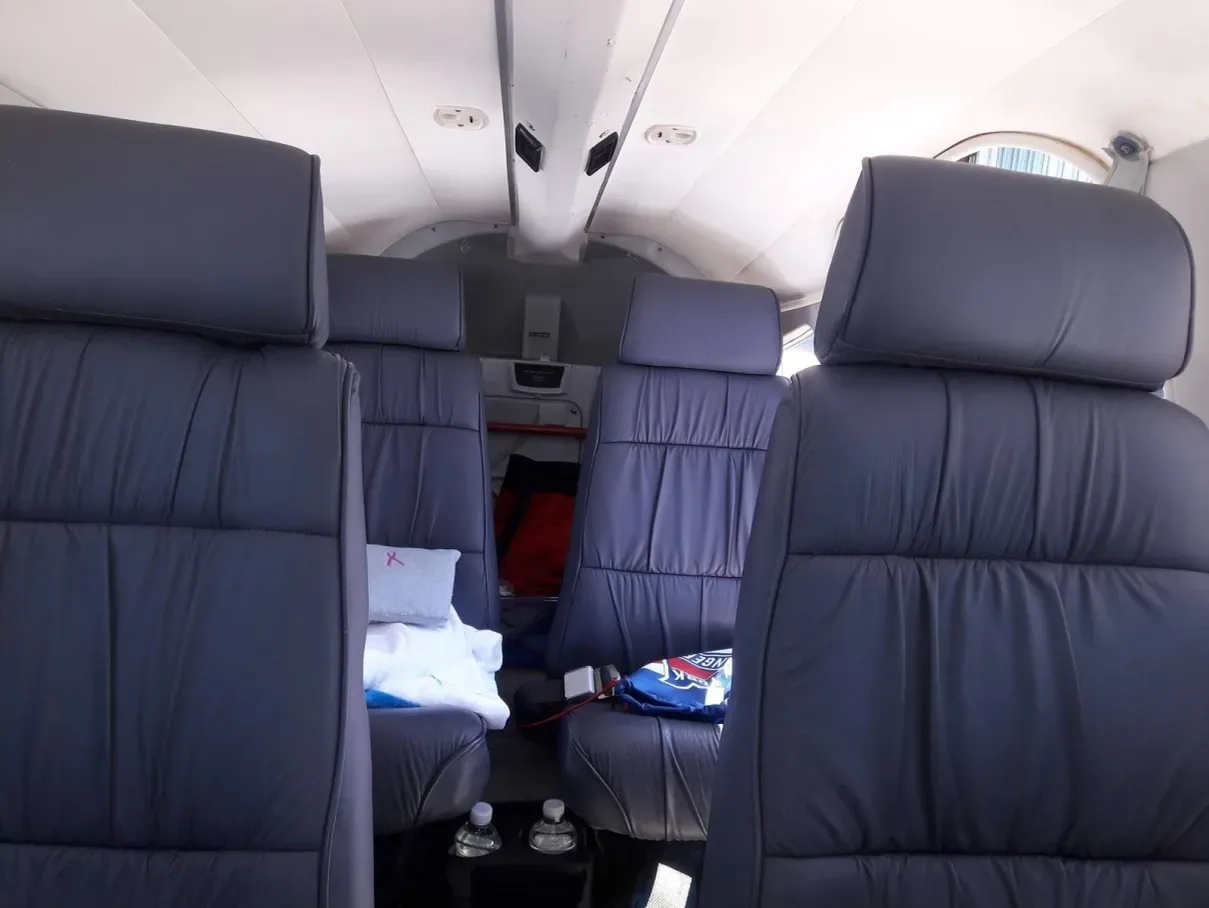 The aircraft cabin interior with four dark grey leather seats and a light-colored ceiling.