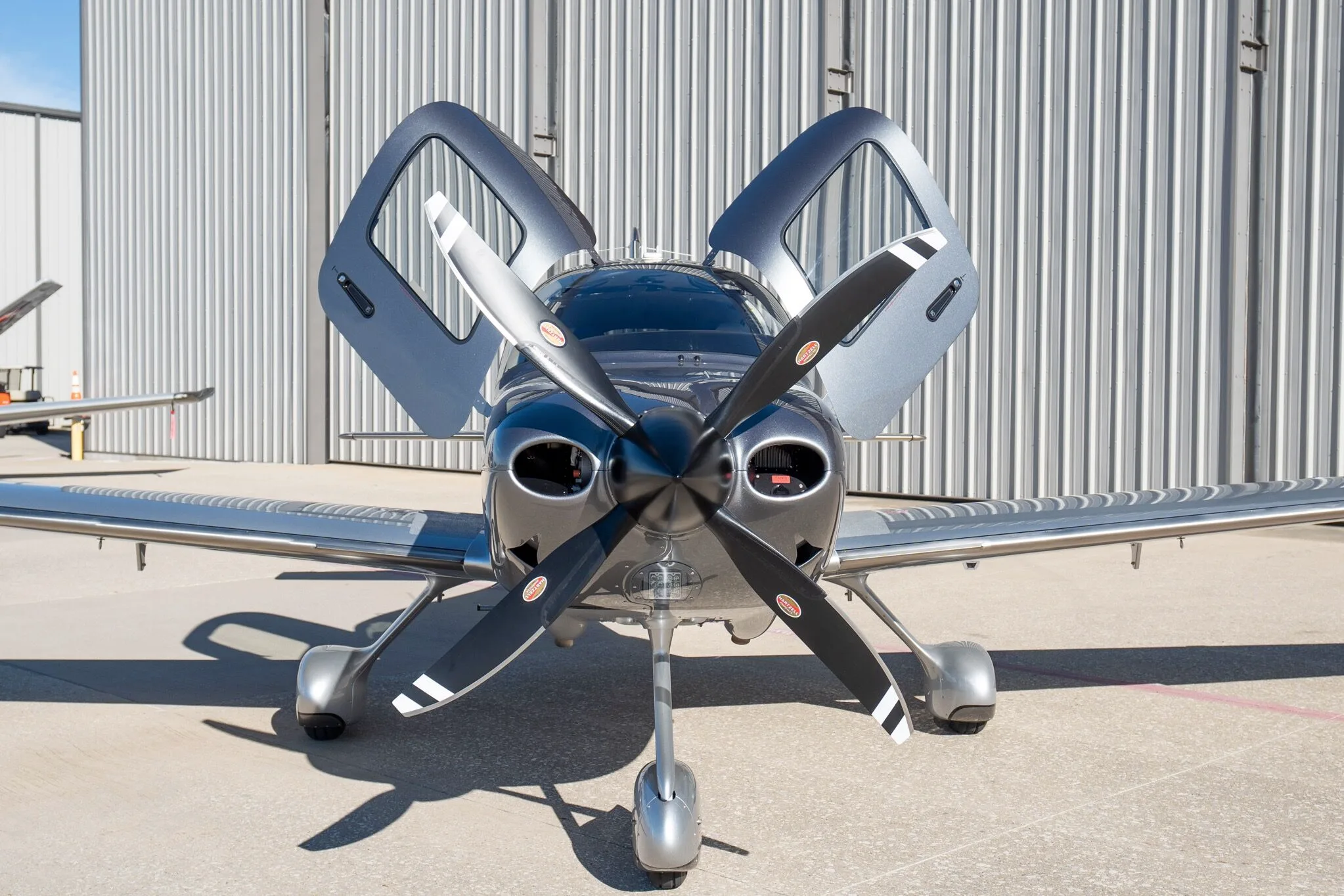 A head-on view of a silver and dark grey Cirrus SR22T Carbon Edition aircraft (N112FS) with its gull-wing doors open.