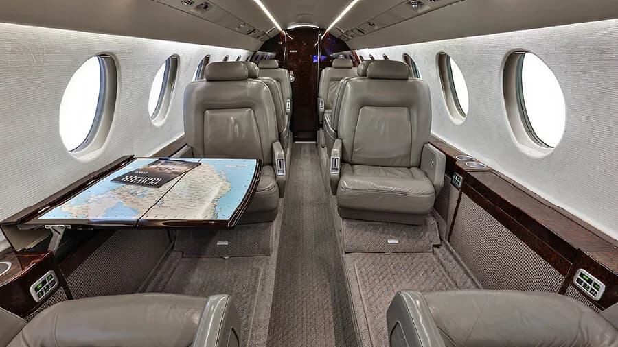 The luxurious cabin interior of a business jet with grey leather seats and a table displaying a map.