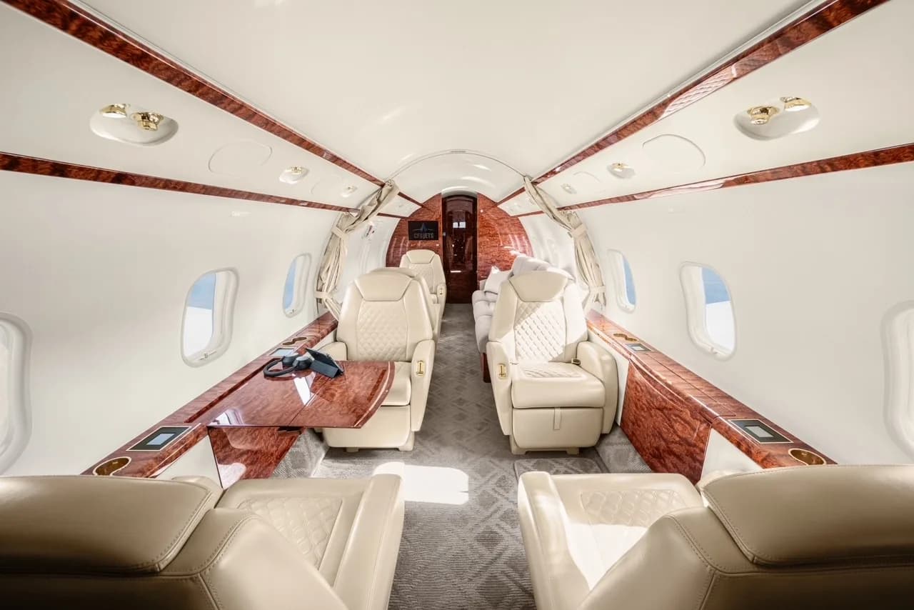 The luxurious cabin interior of a business jet with light cream leather seats and polished wood accents.