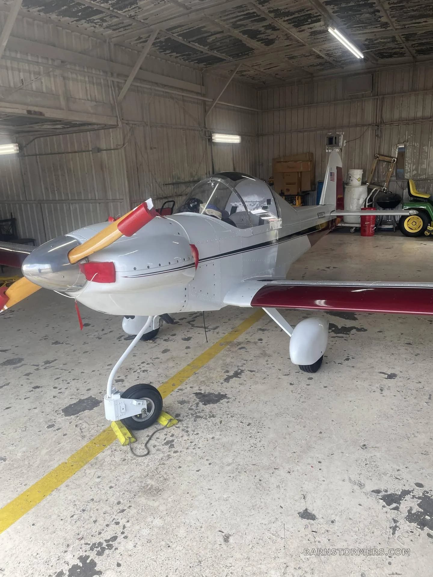 A white and maroon single-engine experimental aircraft with a tailwheel configuration, parked in a hangar.