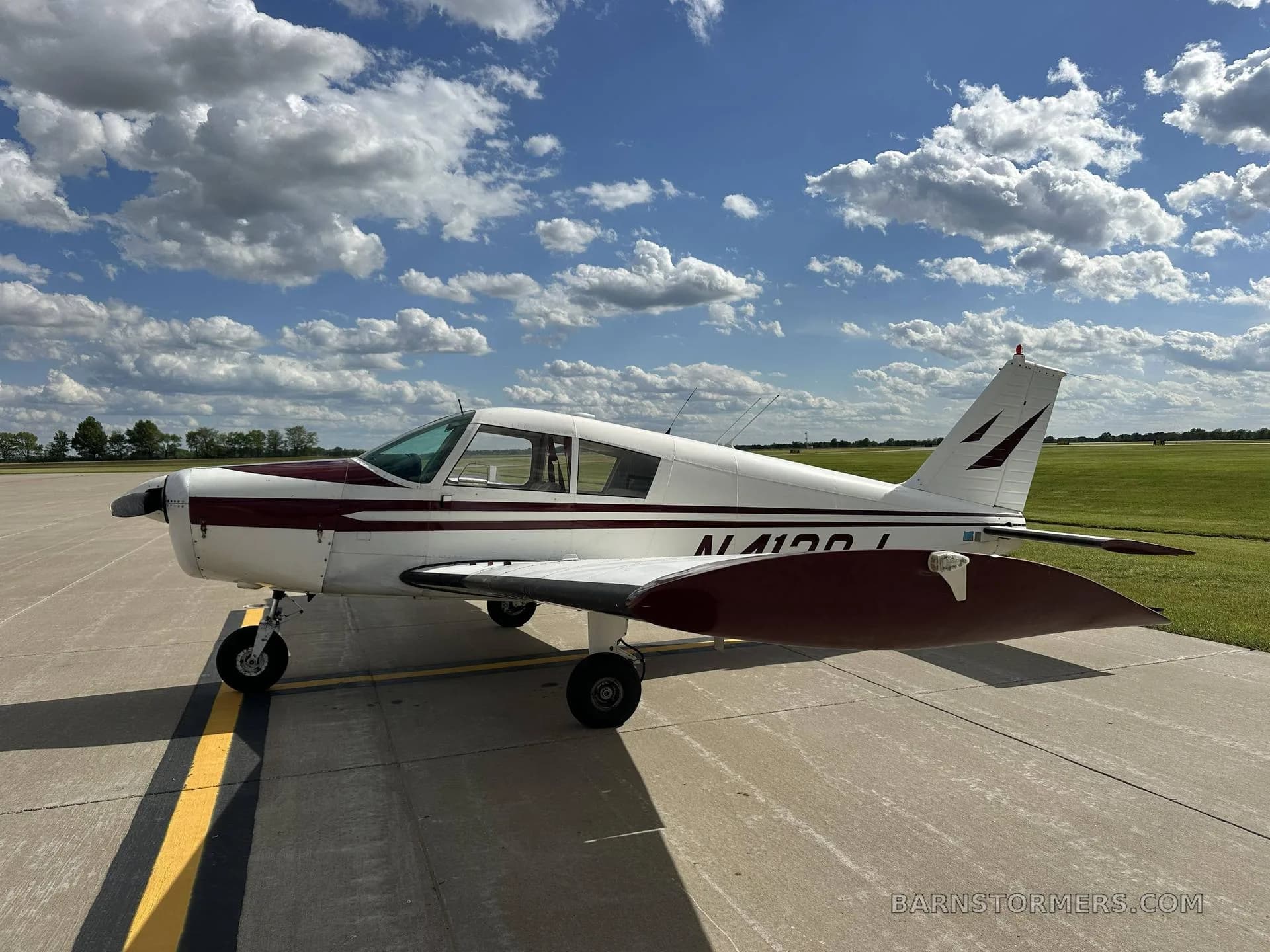 A white and maroon single-engine propeller aircraft, registration N4120J, is parked on an asphalt ramp under a partly cloudy sky, viewed from the left side.