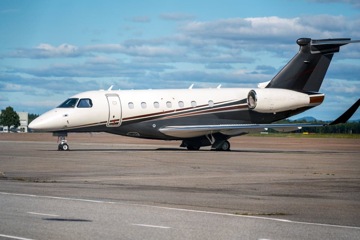 A private jet with a white and brown paint scheme parked on the tarmac.