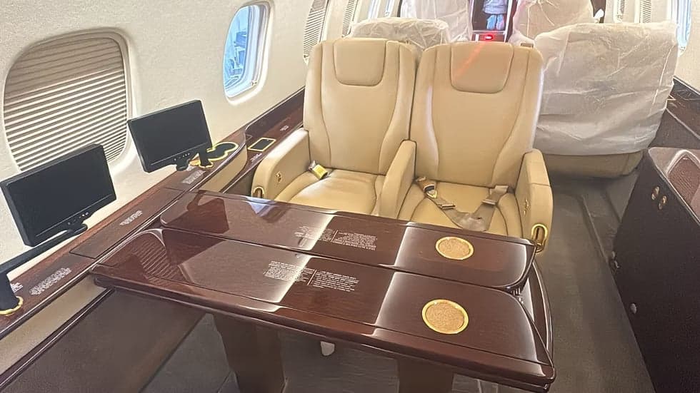 Interior view of the aircraft's cabin with leather seats and fold-out tables.