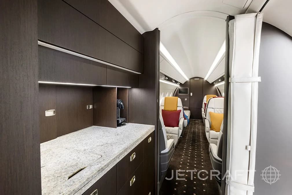 The interior of a jet aircraft with a galley and white leather seats.