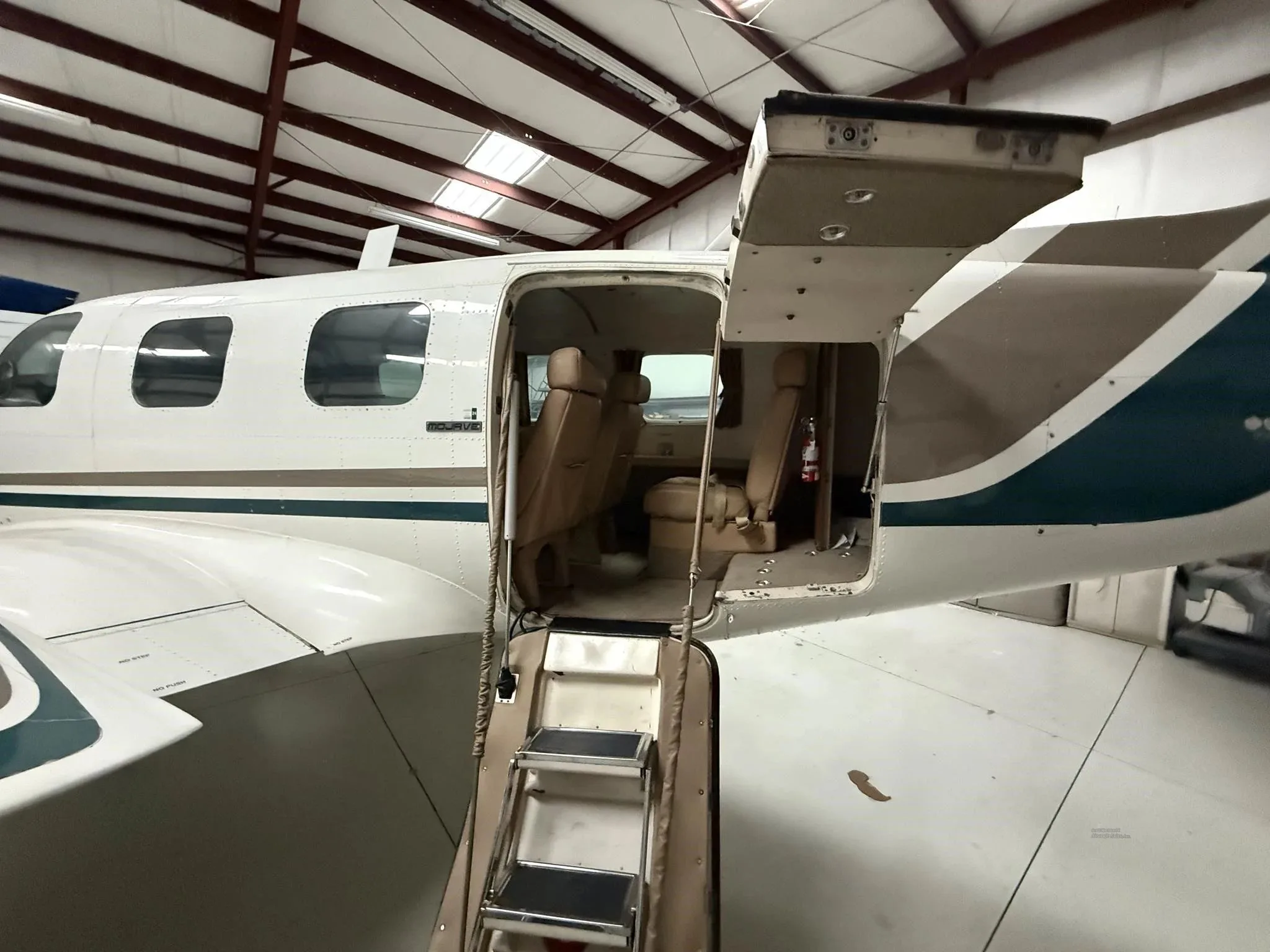 The open passenger door and retractable steps of a Piper Navajo aircraft, showing the tan interior from a wider angle.