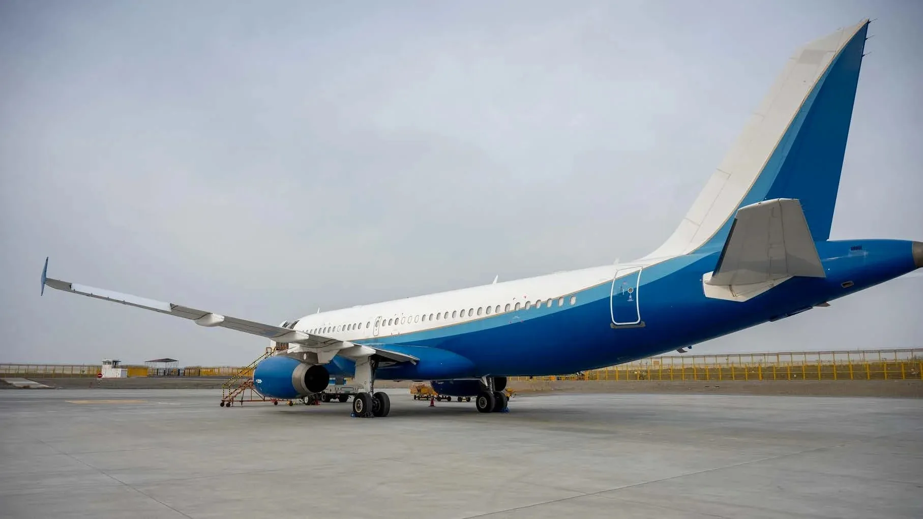 A rear-side view of a white and blue Airbus A320 family aircraft parked on the tarmac.
