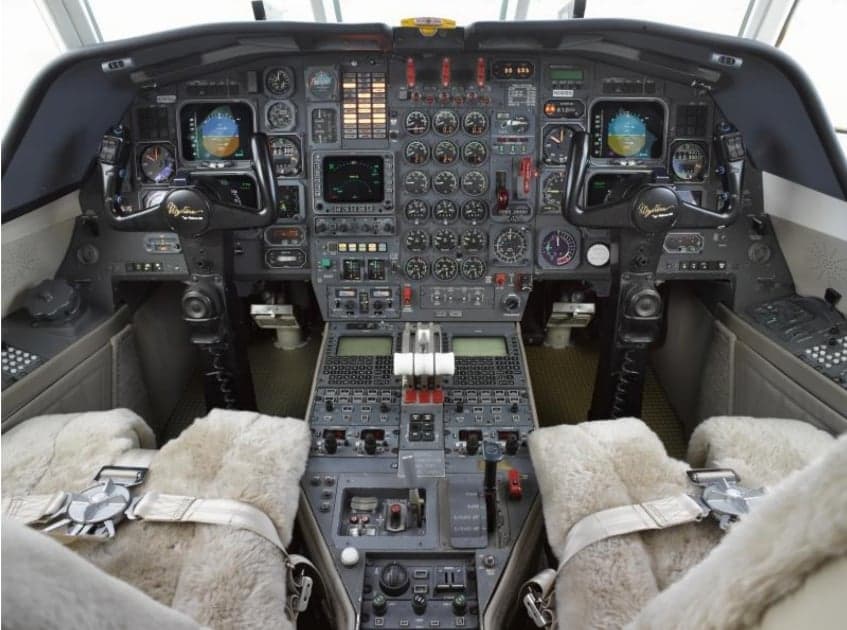 The cockpit of a Falcon jet features a full instrument panel and sheepskin seat covers.