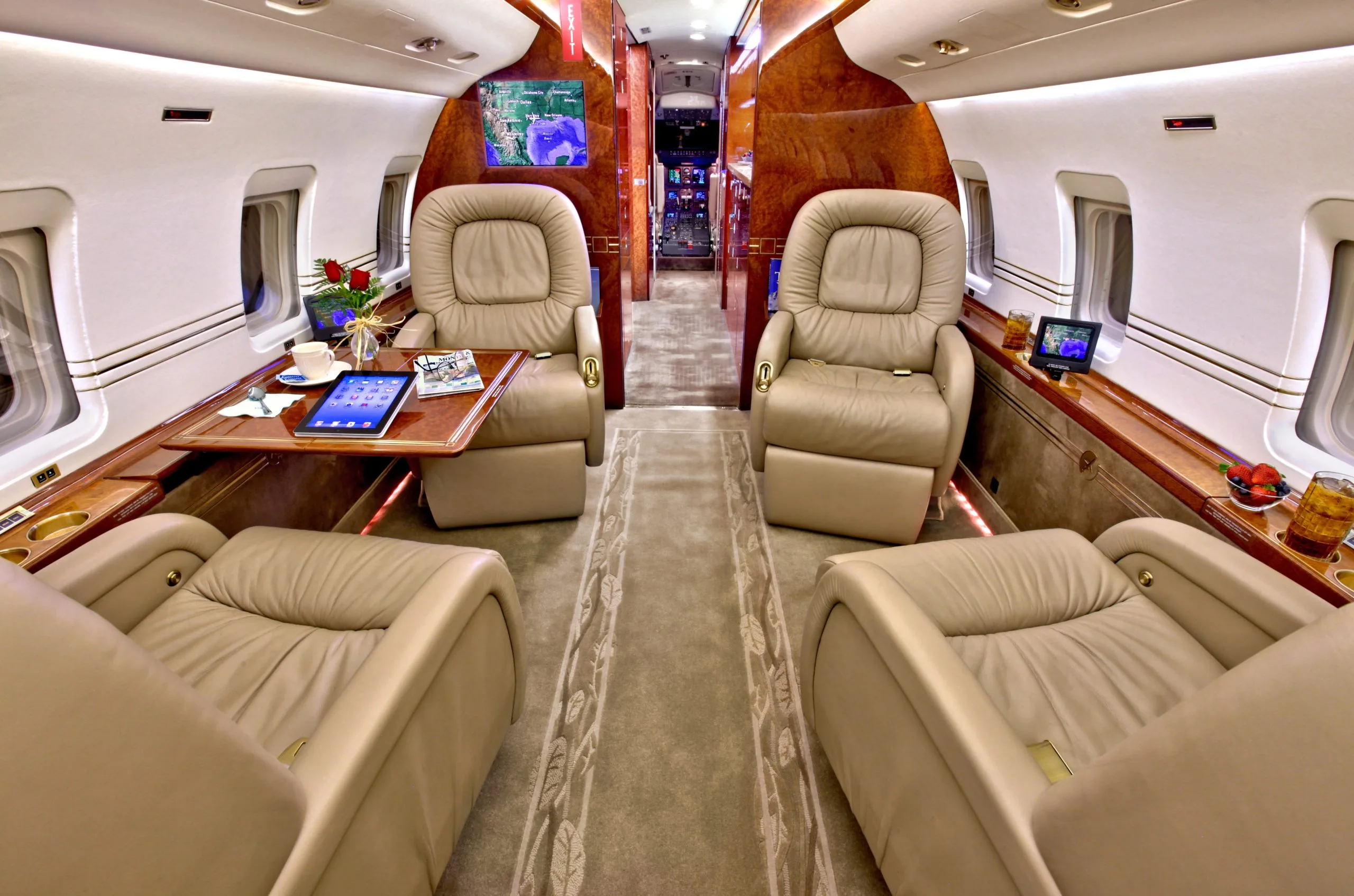 The interior of a private jet cabin featuring beige leather seats and a table with a tablet and coffee.