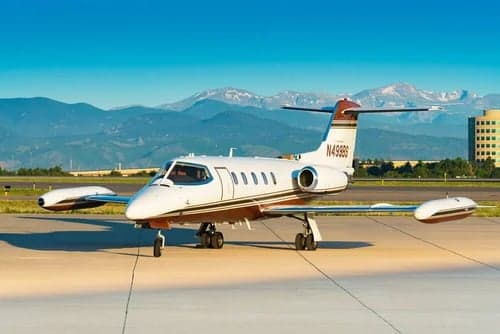 A Learjet 31A with registration N499BS is parked on the tarmac with mountains in the background.