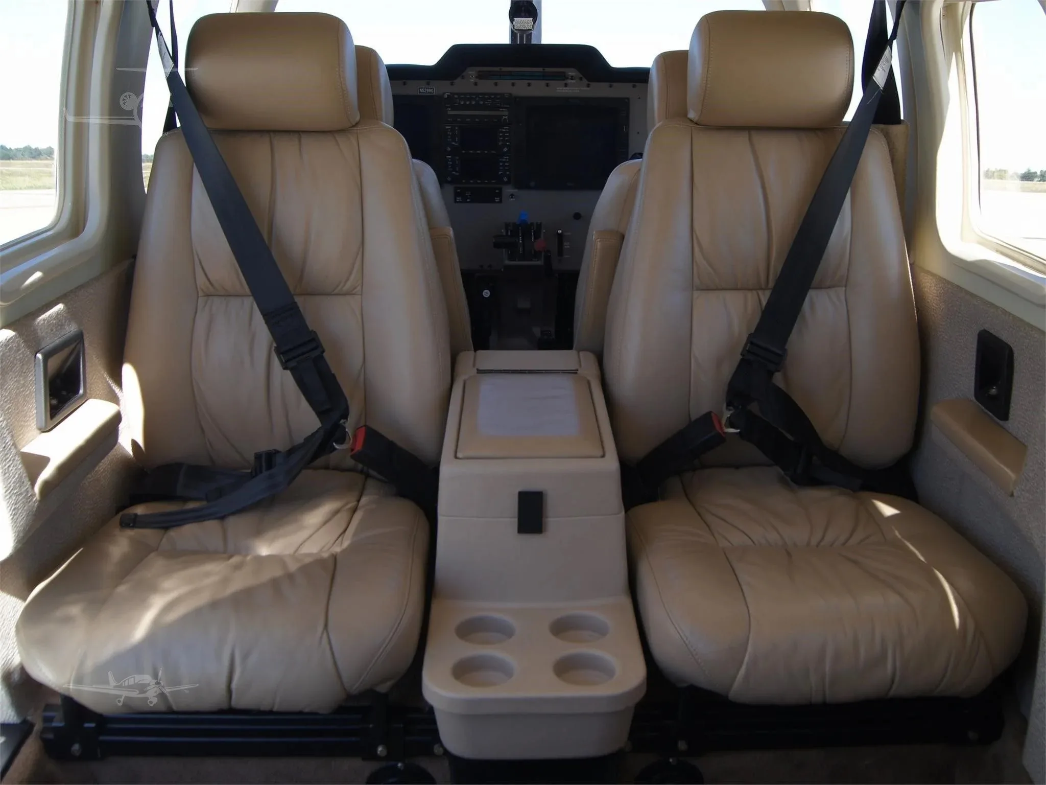 A front-facing view of the two light tan leather passenger seats in the Piper 6XT cabin, with a center console.