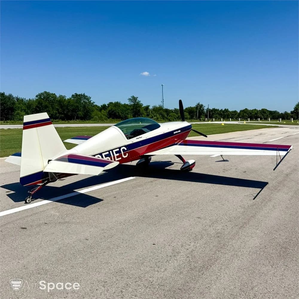 A rear-side view of the red, white, and blue Extra 300L aircraft, N251EC, parked on an asphalt runway.