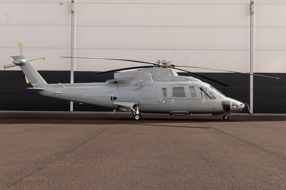 A gray helicopter is parked in front of a building.