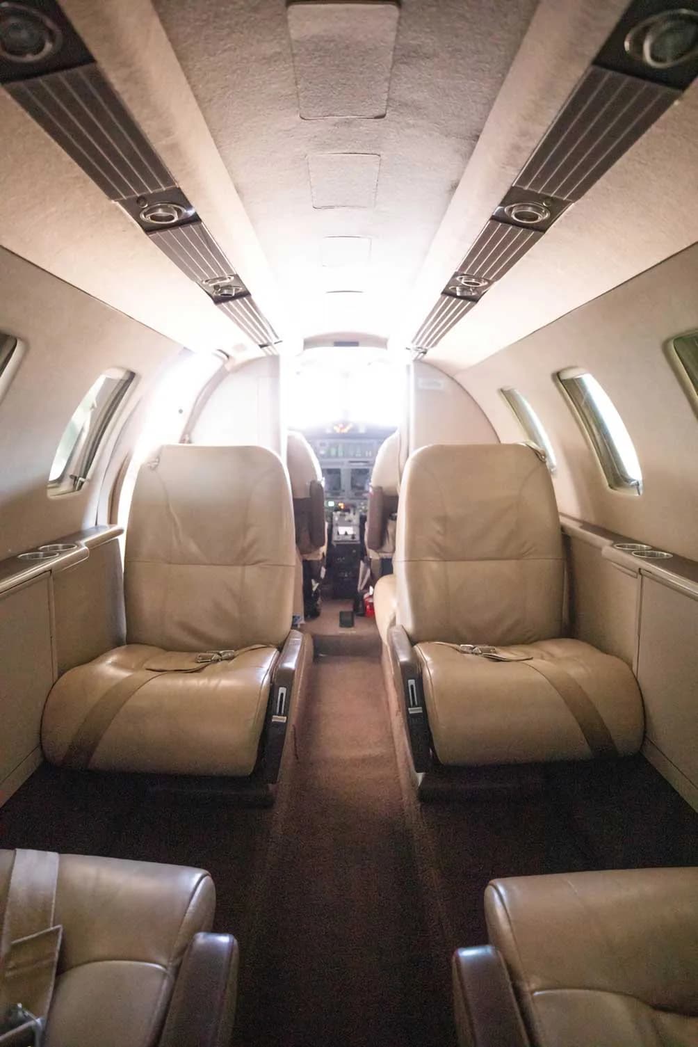 View down the aisle of an aircraft cabin with tan leather seats, looking towards the cockpit.