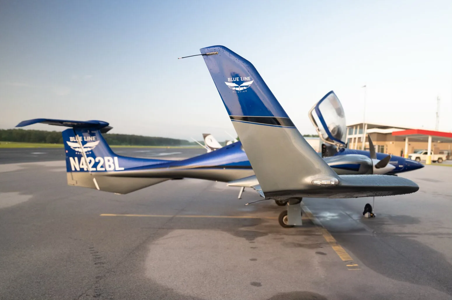Rear view of the blue and grey Diamond DA42NG aircraft, N422BL, with its canopy open on an airfield.