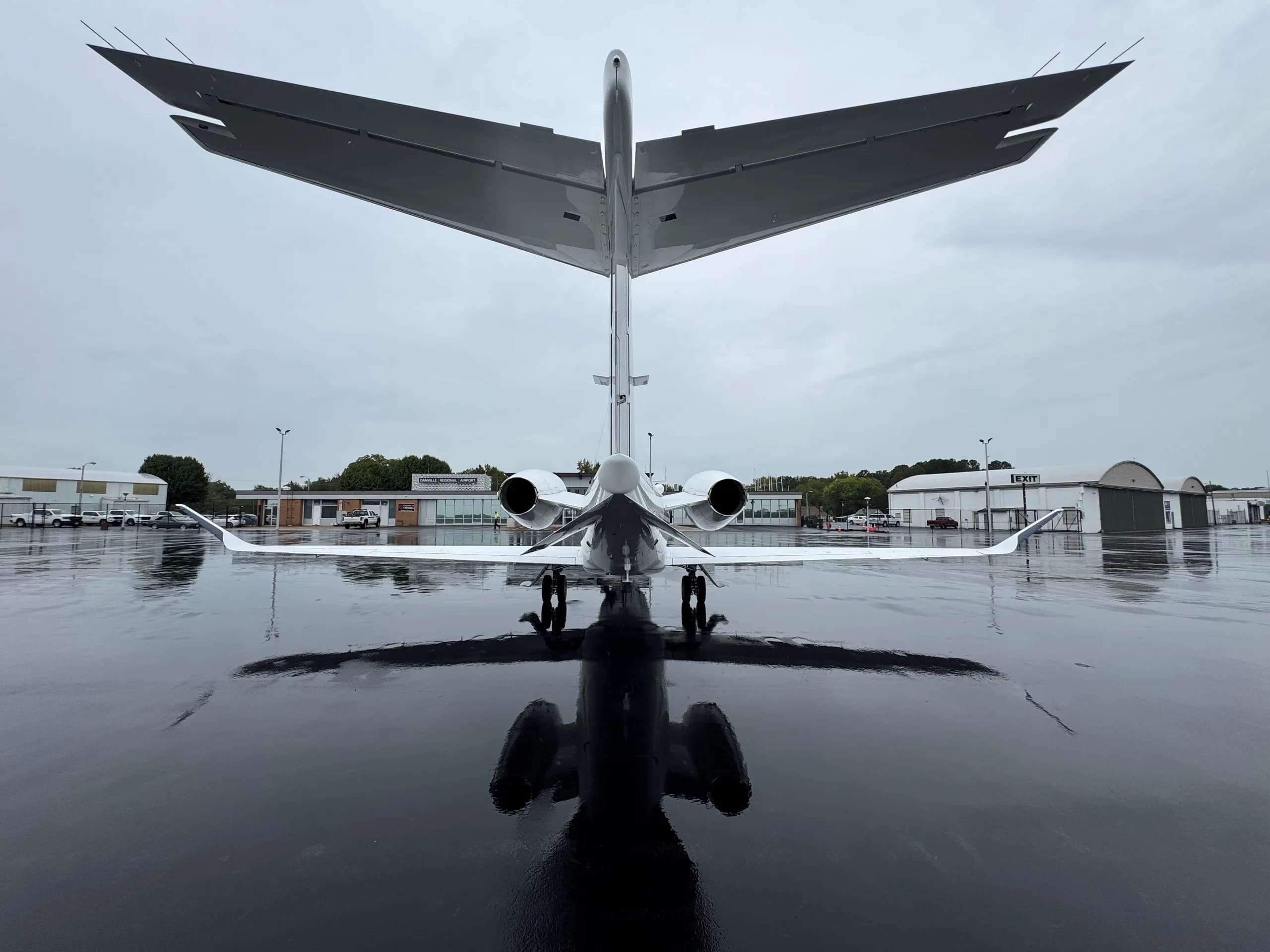 Rear view of a white jet on a wet tarmac, showing the tail and engines.