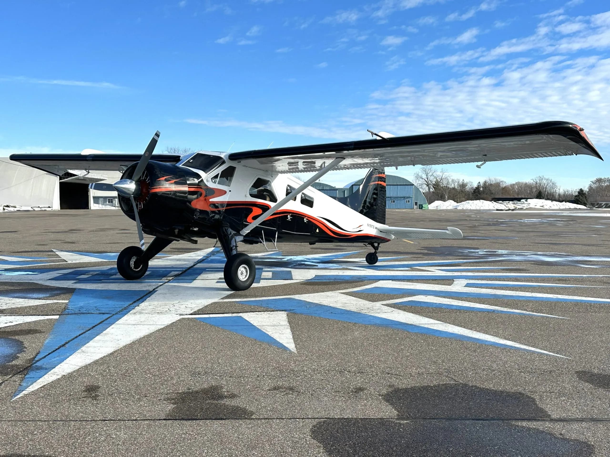 Full side view of a white and black single-engine turboprop aircraft with orange accents parked on an airfield.