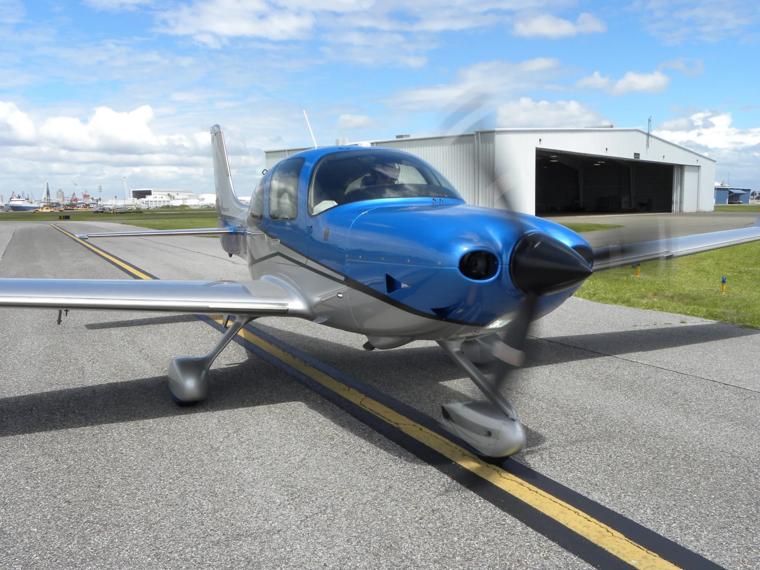 A front-side view of a blue and silver Cirrus SR22T aircraft, N313JB, with its propeller spinning on a taxiway.