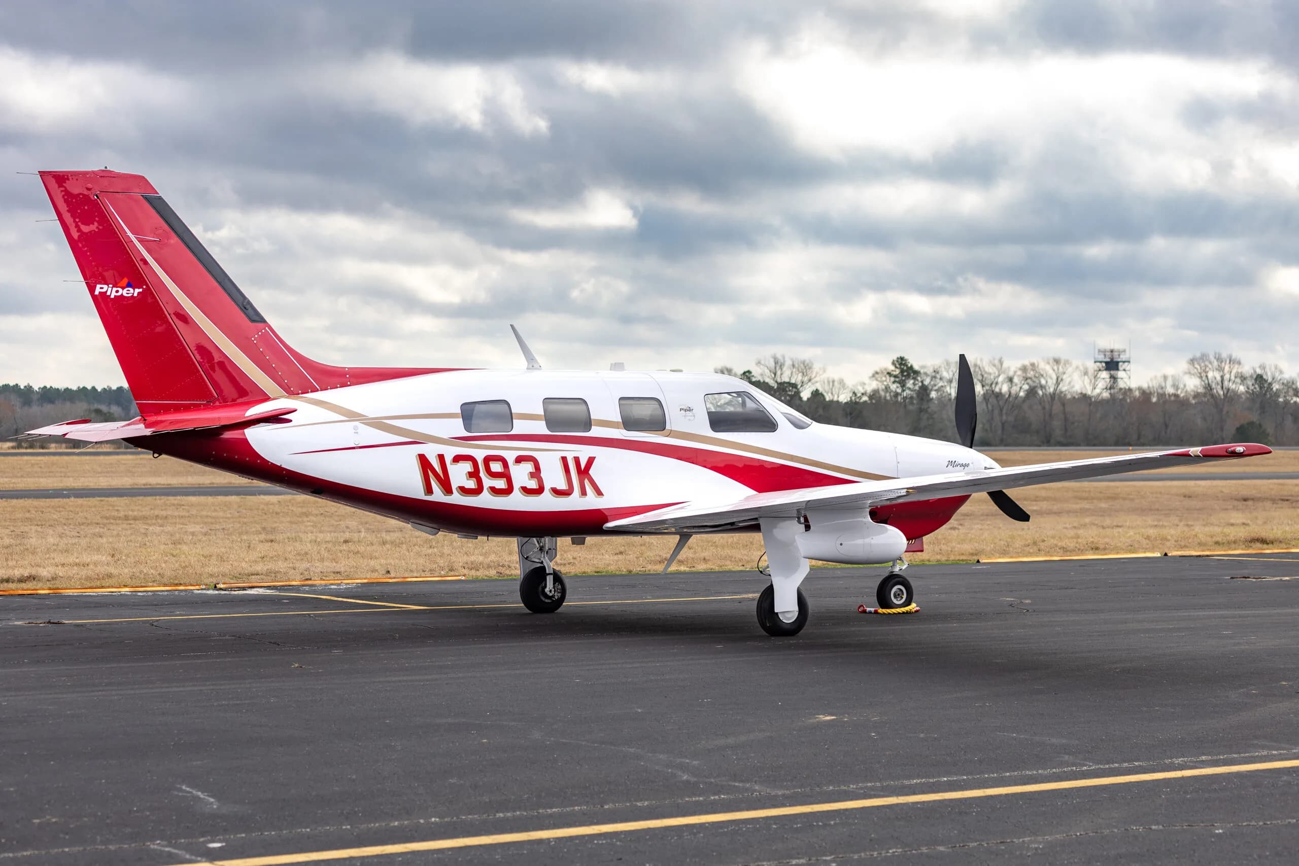 Piper Mirage N393JK on the tarmac, showing its red and white paint scheme against a cloudy sky.