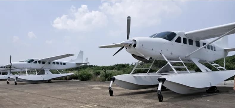 Several white floatplanes are parked on a concrete tarmac under a partly cloudy sky.