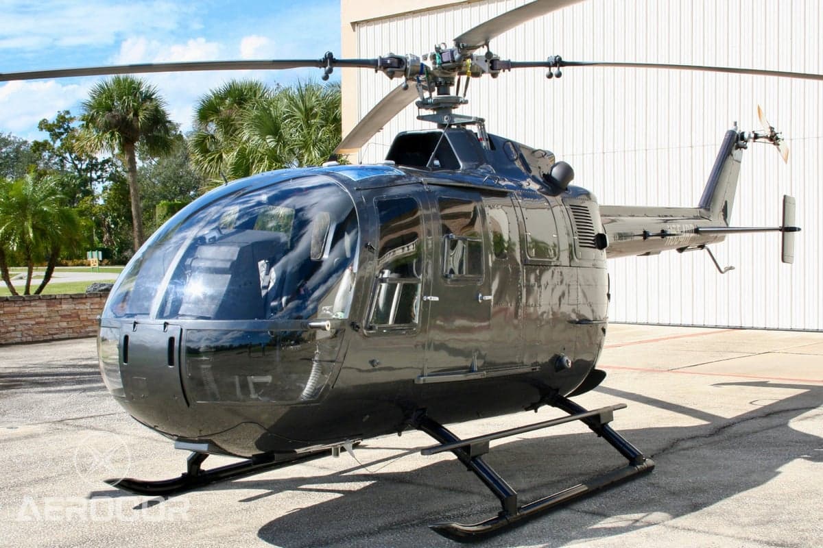 Side view of a black helicopter (N554RP) parked on an apron with palm trees in the background.