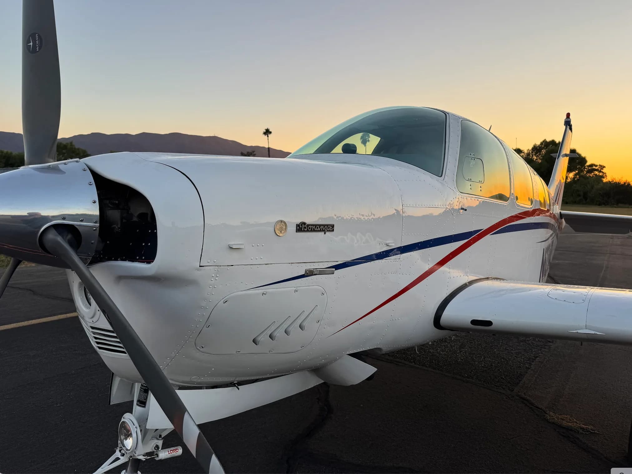 Close-up of the nose of a white and red Beechcraft Bonanza with a mountain backdrop.