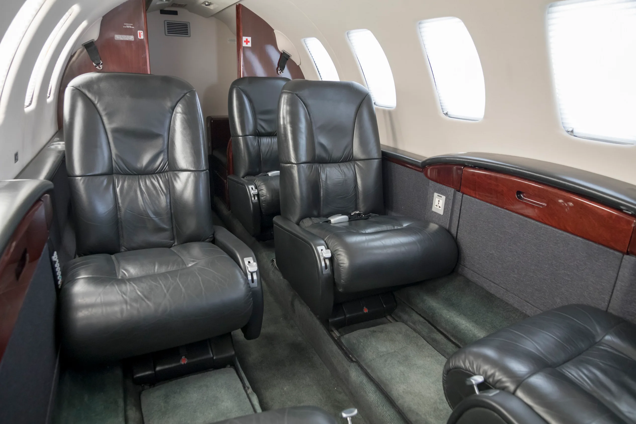 The interior cabin of a private jet with black leather seats and dark wood accents along the side.