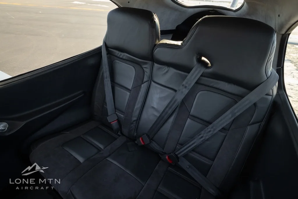 An angled view of the black leather rear seats with seatbelts in the aircraft cabin.