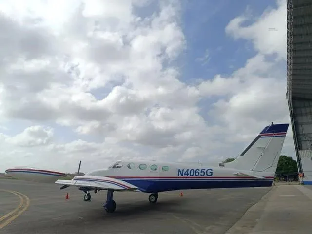 A three-quarter rear view of a white and blue Cessna 340 twin-engine aircraft with red stripes on an airfield.
