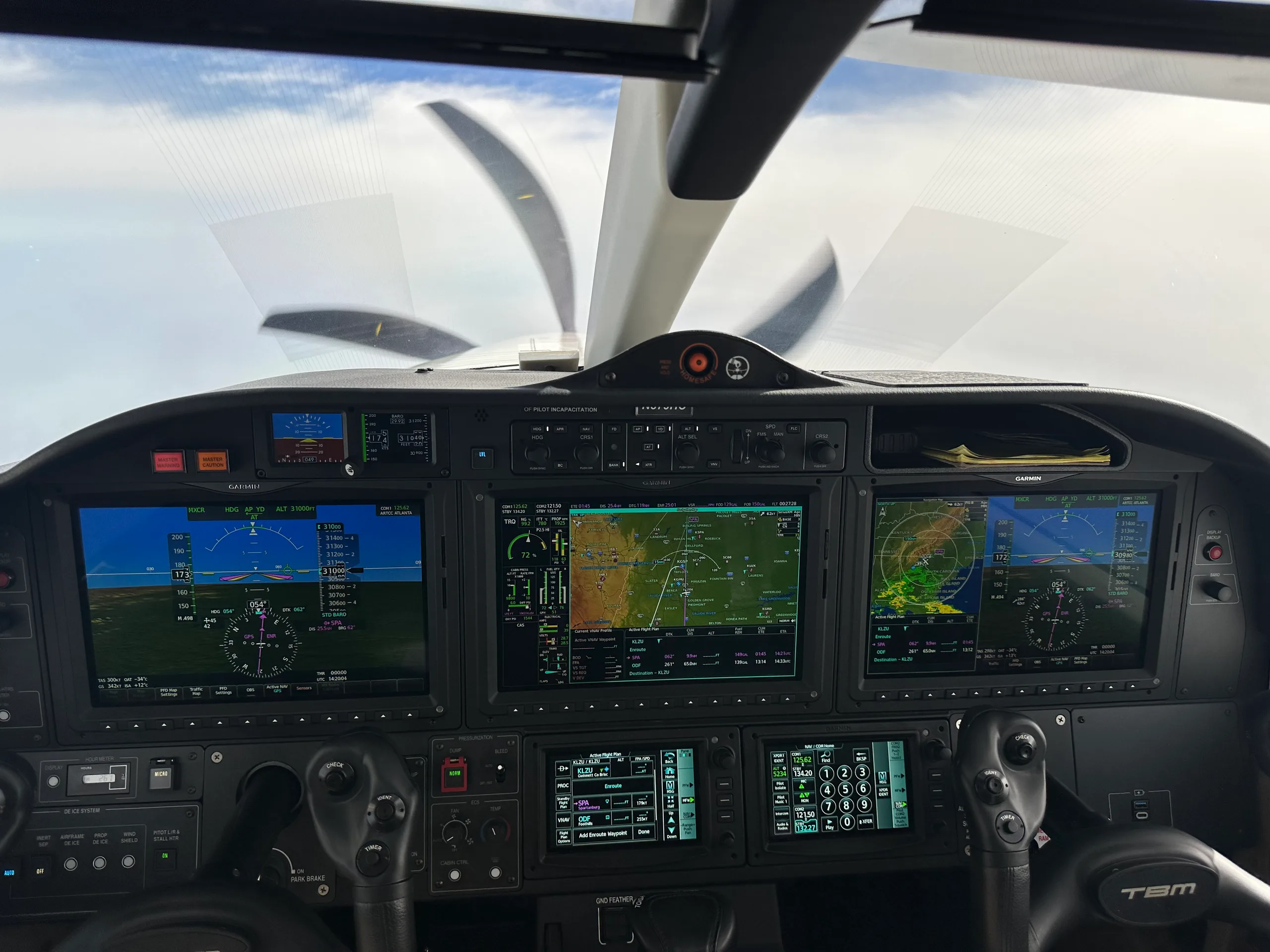 The cockpit of a TBM 960 aircraft, showing multiple glass displays and the propeller through the windshield.
