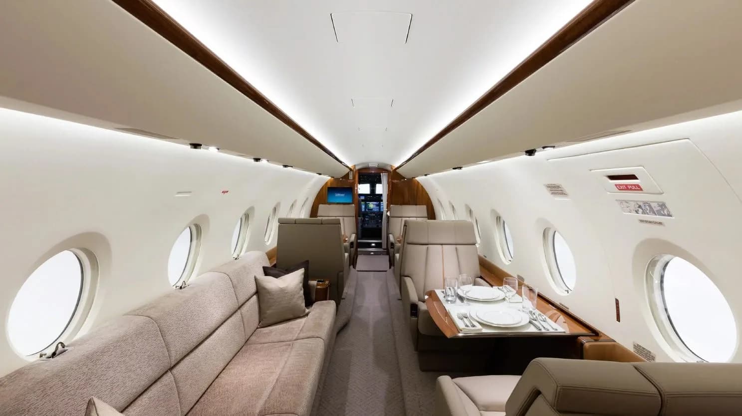A wide view of an aircraft cabin with a long beige sofa, individual seats, and a dining table set for two.