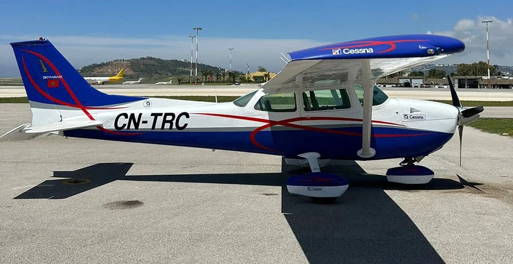 A side view of a blue and white Cessna 172 Skyhawk aircraft with registration CN-TRC parked on an airfield.