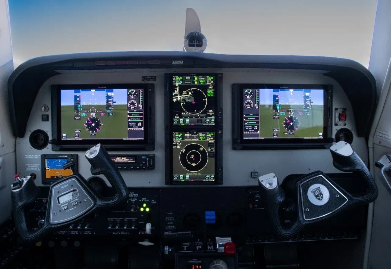 The cockpit of an aircraft featuring a modern glass panel with multiple digital displays and two control yokes.