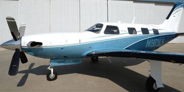A Piper Meridian aircraft with a blue and white paint scheme is parked in front of a hangar.