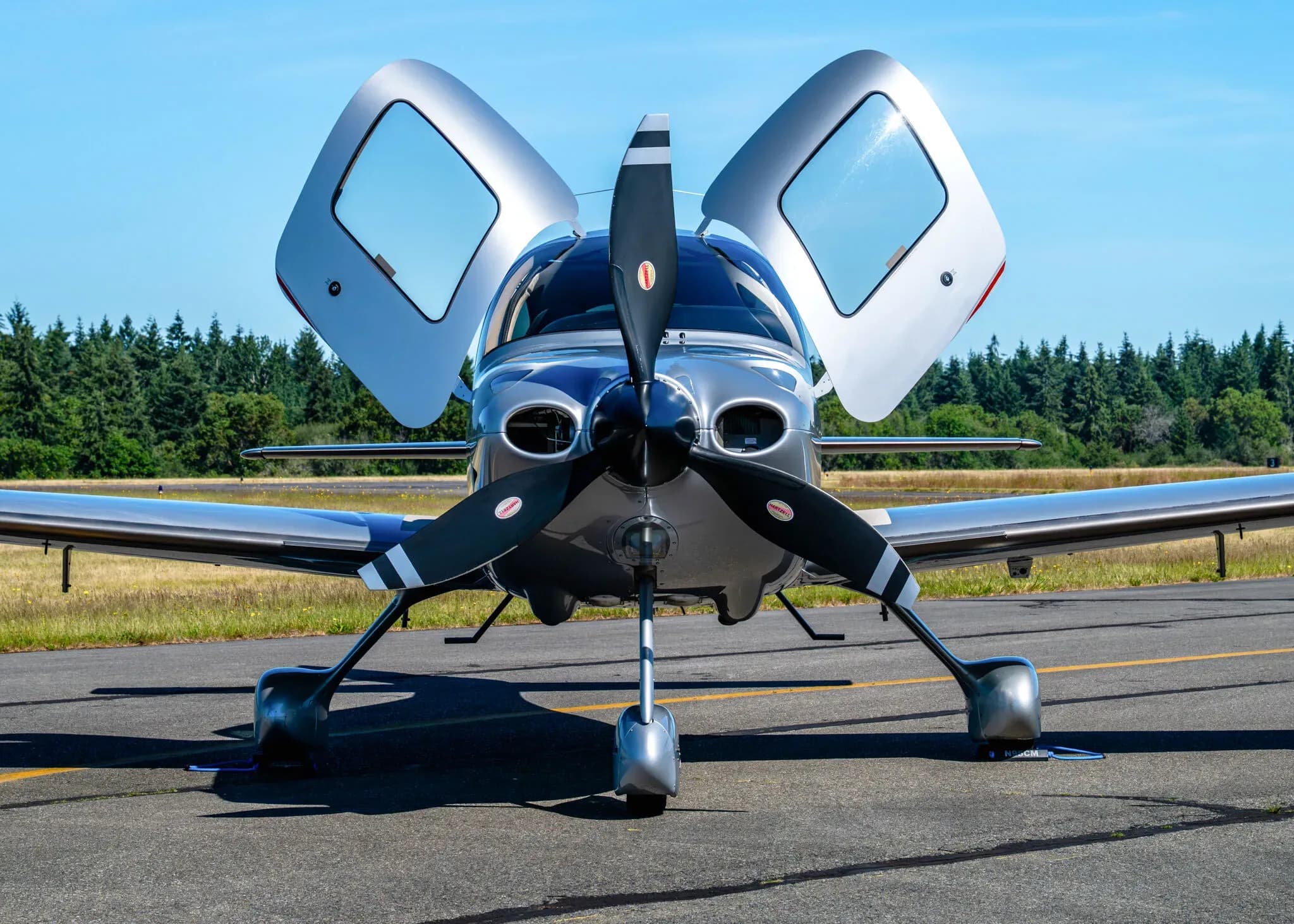 Front view of a silver Cirrus SR22T aircraft with registration N95CM, showing its propeller and open gull-wing doors.
