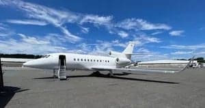 Exterior view of a white Falcon jet parked on the tarmac with the door open.
