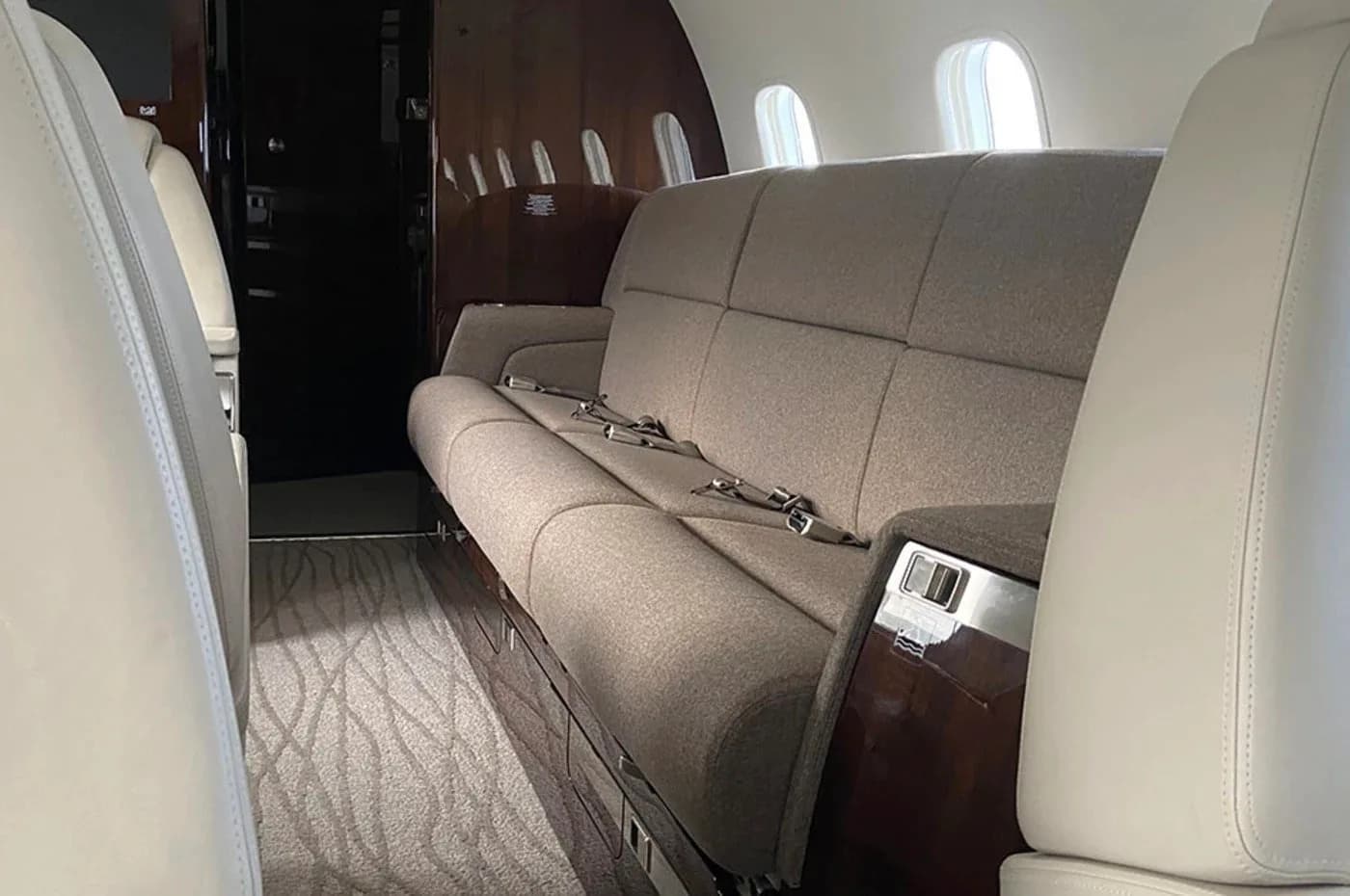 A close-up view of a comfortable brown fabric sofa inside a private jet cabin, with dark wood accents.